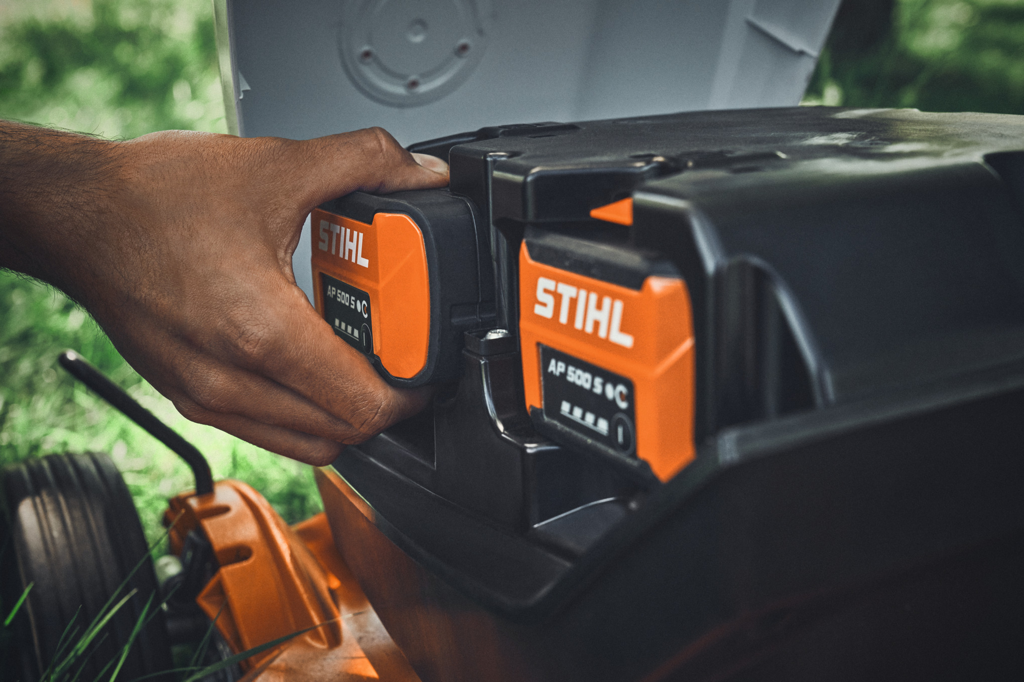Людина вставляє акумулятор STIHL AP 500 S в акумуляторну газонокосарку STIHL