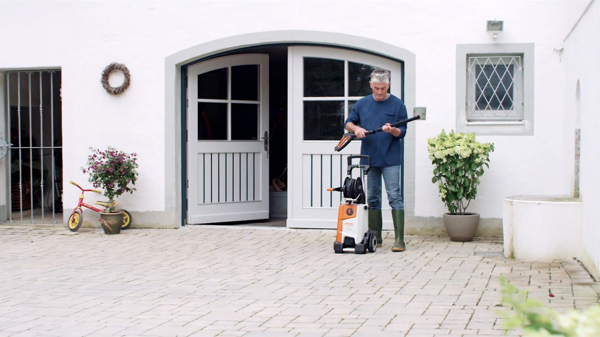 Mann steht vor weißem Haus und bereitet STIHL Hochdruckreiniger vor, um Fassade zu reinigen