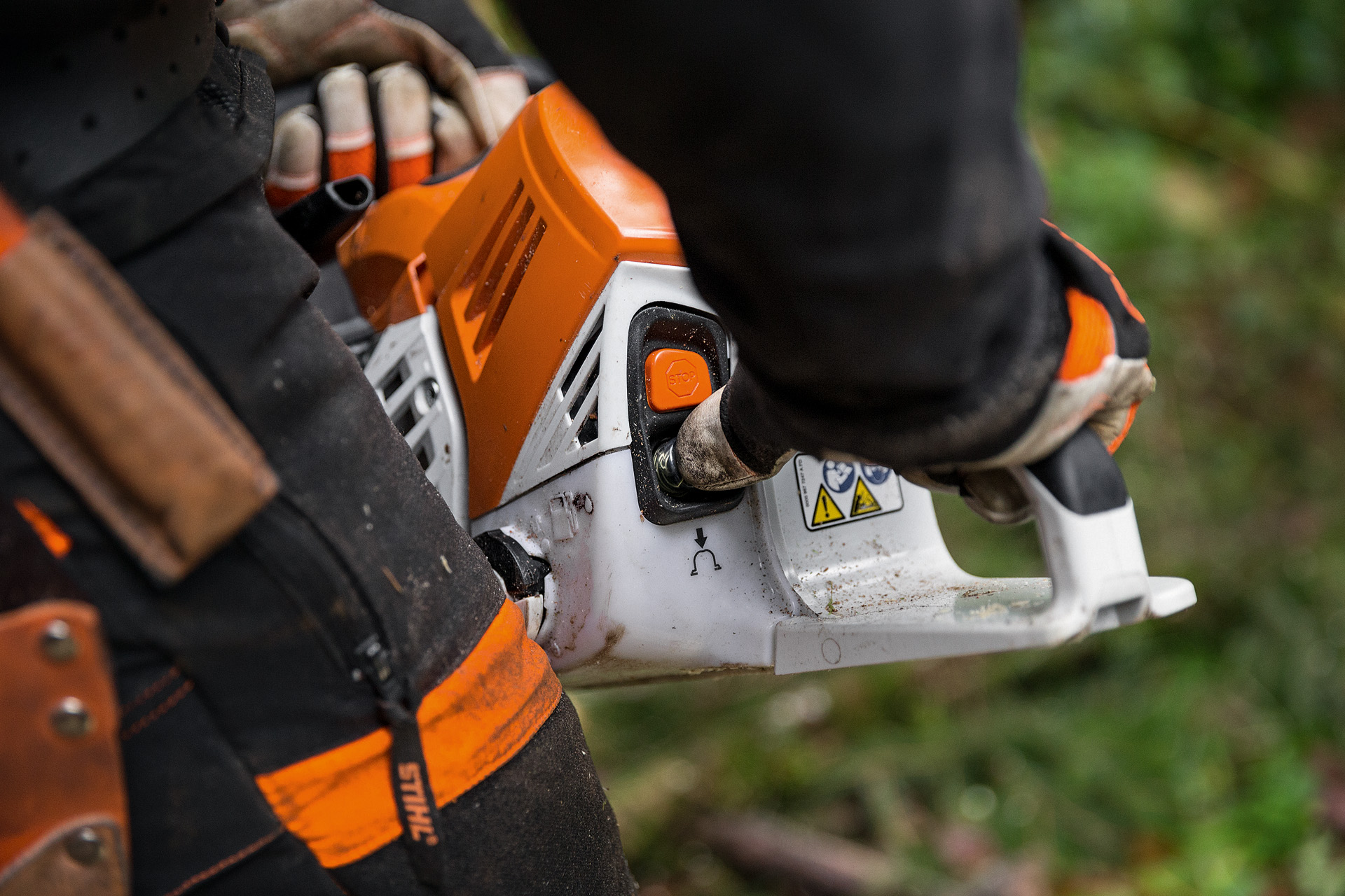 Людина у захисному одязі запускає бензопилу STIHL MS 500i на землі в листяному лісі