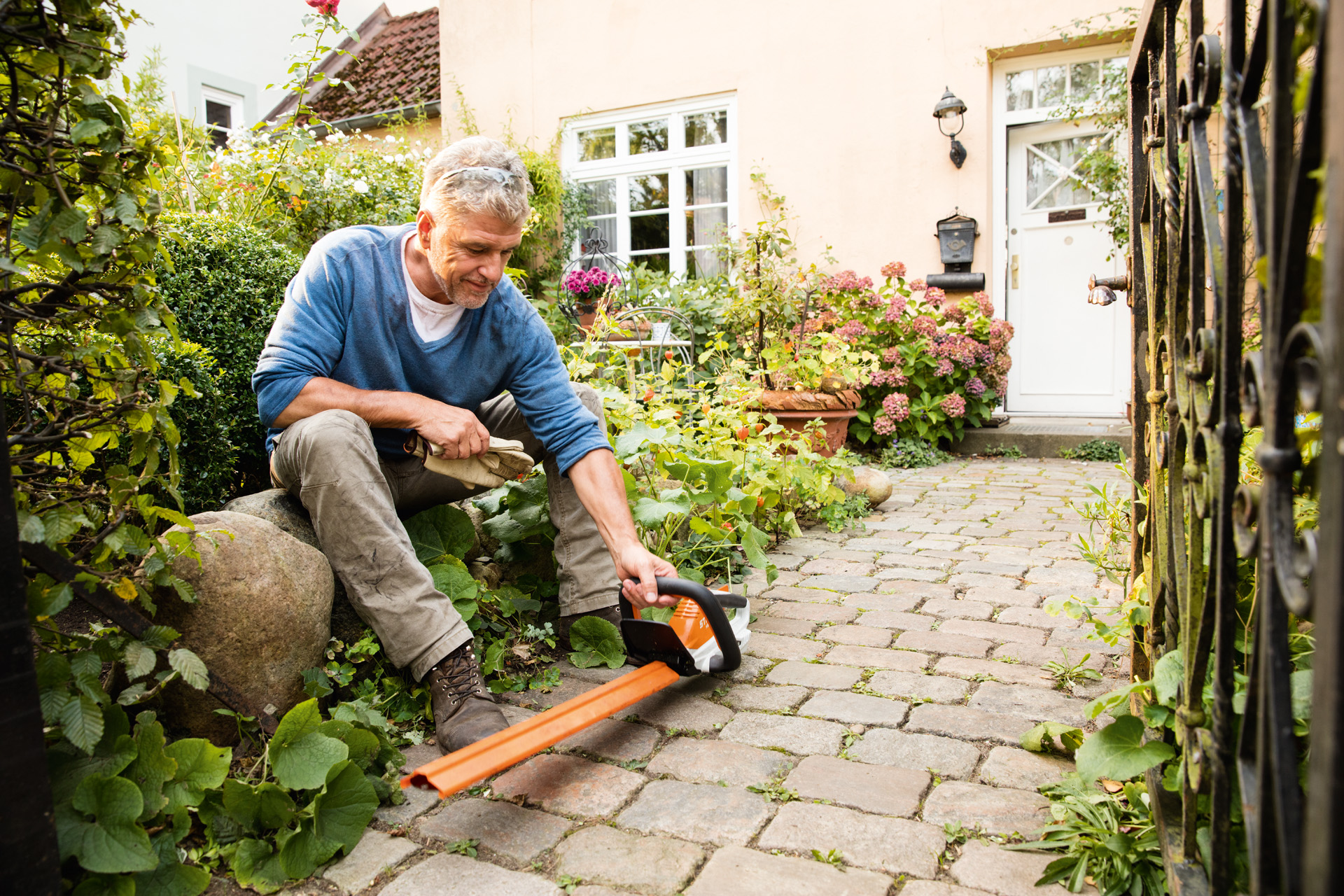 Чоловік з електричними мотоножицями STIHL HSA 45 з лінійки AI перед будинком