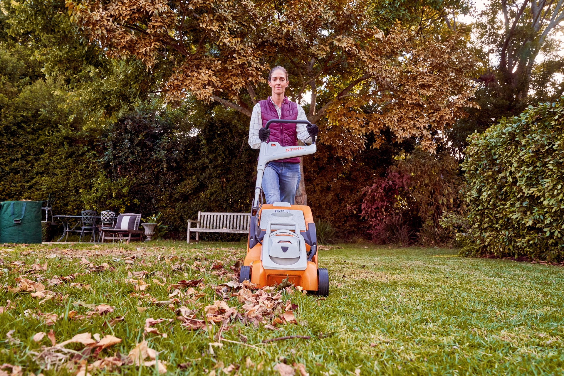 Frau betreibt mit STIHL Akku-Rasenmäher RMA 339 C in einem Garten Rasenpflege im Herbst